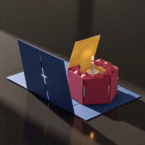 birthday cake GIF — pink paper cake rising from an open blue pop-up card with a candle cutout